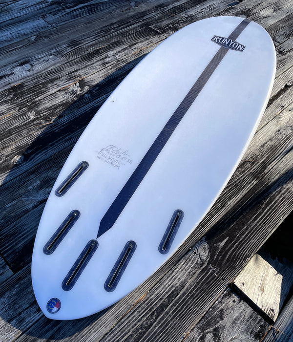 White Surfboard, laying on wood deckings. 4 Plus 1 fun setup. Future Fin Boxes. "Fully Auto" is penciled in under autograph.