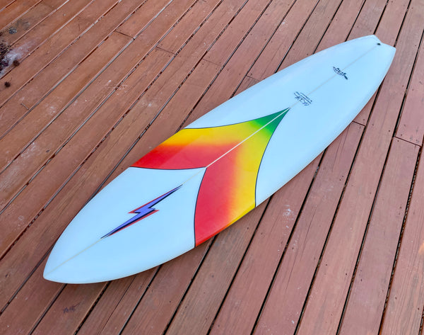 white and multi colored mid length swallow tail surfboard