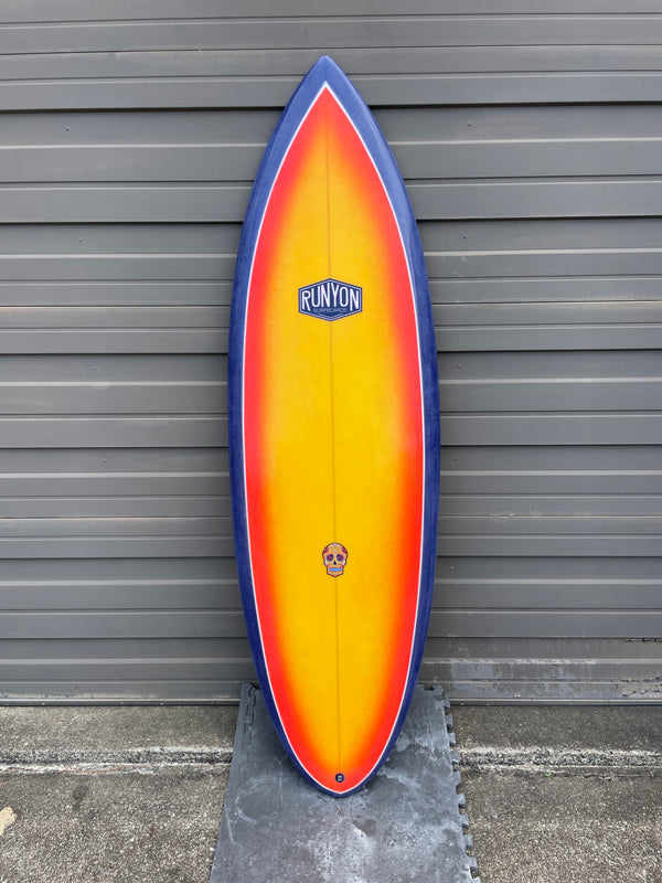 Surfboard Standing against sheet metal wall, blue edges, sunset yellow to orange gradient in the center. Runyon logo on the top.
