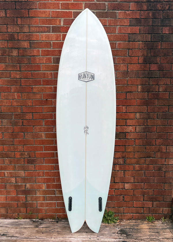 White King Fish surfboard leaning against a brick wall. Runyon logo in the center. Twin Fin setup, with Future Fin Boxes.