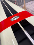 A red and black Runyon surfboard with white stripes, seen from an overhead angle among other surfboards in a shop or storage area.