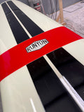A red and black Runyon surfboard with white stripes, seen from an overhead angle among other surfboards in a shop or storage area.