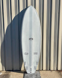 The image shows a white surfboard with the brand name "Runyon" printed on it. The board has a distinct single fin design and appears to be a high-quality, professionally shaped surf craft. The background shows a corrugated metal or wood siding, suggesting the surfboard is resting against a wall or structure.