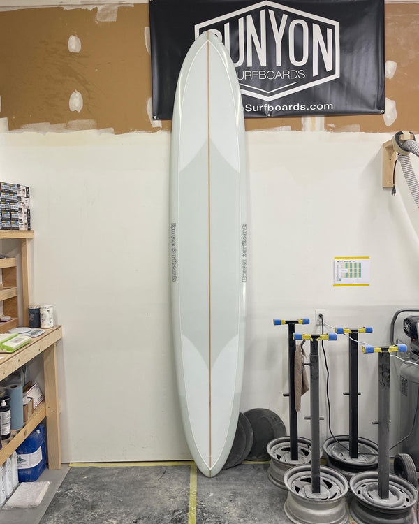 A gray framed, white glider longboard, leaning against a wall. Runyon Banner hanging behind. 