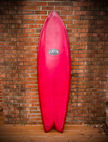 Rouge King Fish Surfboard, leaning against a brick wall. Runyon logo in the center. 
