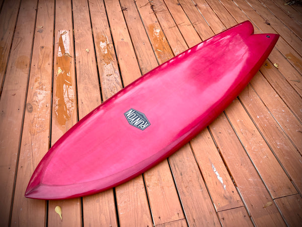 Rouge King Fish Surfboard laying on a wooden deck. Runyon logo in the center. Fish Shaped design. 