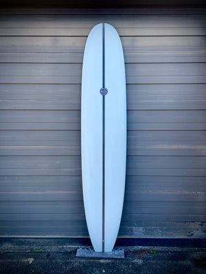 A white surfboard with a logo leaning against a sheet metal wall.