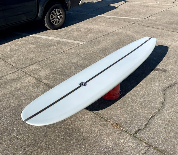 A white surfboard with a black logo resting on a concrete surface.