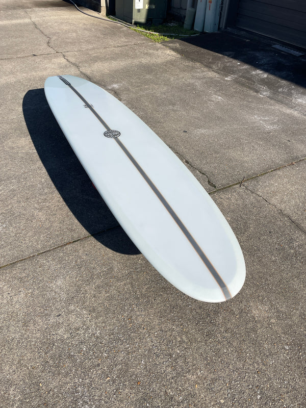 A white surfboard with a black logo resting on a concrete surface.