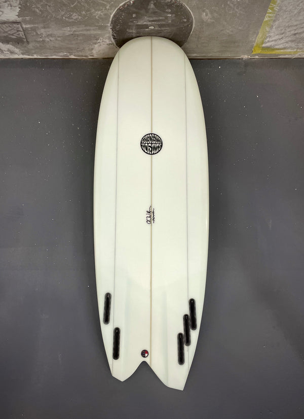 White, Asymmetric Mini Hammer Surfboard laying on its deck. 2 Fin Boxes on the left side of the fishtail, 3 fin boxes on the right. 