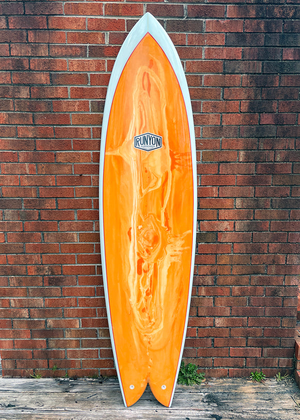 King Fish Surfboard, Orange and White Swirled design, with white frame. Leaning against a brick wall. 