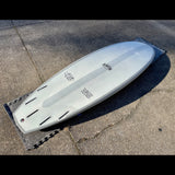 The image depicts a white Runyon surfboard resting on a concrete surface. The board has a clean, minimalist design without any graphics or logos, aside from the Runyon brand name.